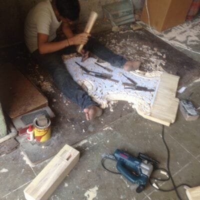 A carver shaping a panel by hand with mallet and chisel